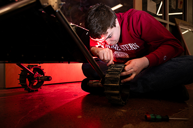 a young student sits on the floor working on a robot