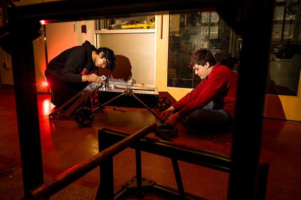 two young students sitting on the floor working on a robot
