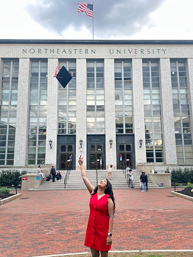pattala standing outside Northeastern Ell Hall throwing her graduation cap
